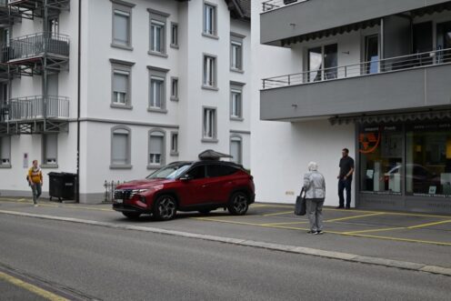 Auto ohne Lenker fährt aus Parklücke, zwei Fussgänger sind sich am annähern